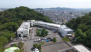丘陵地に建つ介護施設の全景。周辺の緑に囲まれた立地環境が見える。